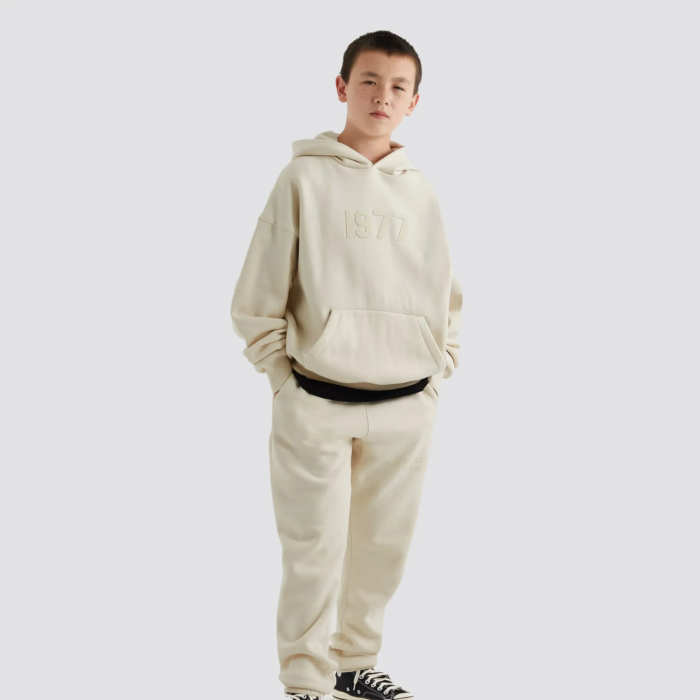 The Fear of God Essentials Kids Tracksuit in cream is a stylish and comfortable tracksuit set for children. It is made by Fear of God, a luxury fashion brand known for its street-inspired and casual designs. The tracksuit is made of a comfortable and durable fabric, and comes in a cream color. The set includes a full-zip hoodie and pants with ribbed cuffs and hem for a snug fit. The tracksuit often features the brand's logo on the chest. The cream color gives it a clean and timeless look, perfect for any occasion.